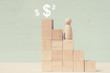 © gesrey - Wooden figure climb to upper stage above which are drawn dollar signs.