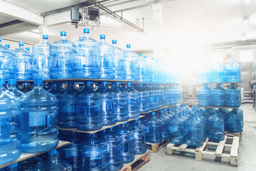 Wall Mural - Gallons or plastic bottles of purified drinking water on pallets in water production factory interior inside in sunlight