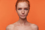 Fototapeta  - Studio photo of beautiful young readhead female with casual hairstyle standing over orange background without clothes, looking at camera with calm face