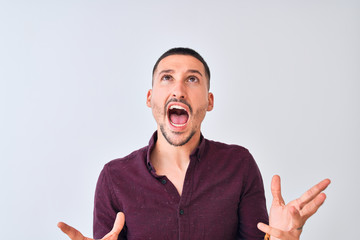 Sticker - Young handsome business man standing over isolated background crazy and mad shouting and yelling with aggressive expression and arms raised. Frustration concept.