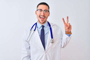 Sticker - Young doctor man wearing stethoscope over isolated background smiling with happy face winking at the camera doing victory sign with fingers. Number two.