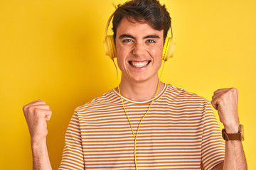 Sticker - Teenager boy wearing headphones over isolated yellow background celebrating surprised and amazed for success with arms raised and open eyes. Winner concept.