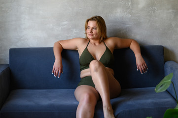  Beautiful plump woman in a beige swimsuit sitting on a sofa