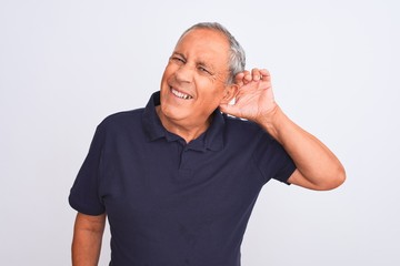 Canvas Print - Senior grey-haired man wearing black casual polo standing over isolated white background smiling with hand over ear listening an hearing to rumor or gossip. Deafness concept.