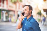 Fototapeta Miasto - Middle age handsome businessman standing on the street talking on the smartphone smiling