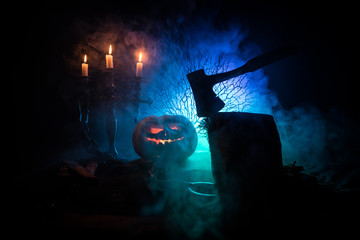 Wall Mural - Scary orange pumpkin with carved eyes and a smile with burning candles and an ax