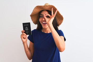 Wall Mural - Beautiful tourist woman wearing hat holding USA passport over isolated white background with happy face smiling doing ok sign with hand on eye looking through fingers