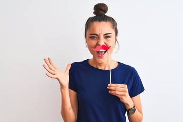 Wall Mural - Young beautiful woman holding fanny party mustache over isolated white background very happy and excited, winner expression celebrating victory screaming with big smile and raised hands