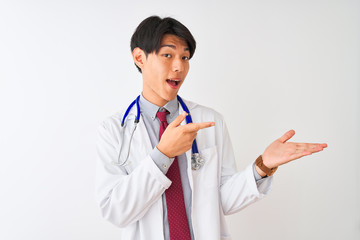 Wall Mural - Chinese doctor man wearing coat tie and stethoscope over isolated white background amazed and smiling to the camera while presenting with hand and pointing with finger.