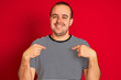 © Krakenimages.com - Young man wearing striped navy t-shirt standing over isolated red background looking confident with smile on face, pointing oneself with fingers proud and happy.
