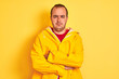 © Krakenimages.com - Young man wearing rain coat standing over isolated yellow background skeptic and nervous, disapproving expression on face with crossed arms. Negative person.