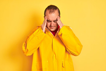 Sticker - Young man wearing rain coat standing over isolated yellow background with hand on head for pain in head because stress. Suffering migraine.