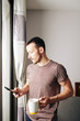 © DragonImages - Handsome young man in t-shirt drinking big mug of coffee and looking at photos of friends on social media