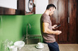 © DragonImages - Man leaning on kitchen counter and using mobile application to order food delivery