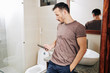© DragonImages - Fit handsome young man hiding in bathroom when texting to another woman