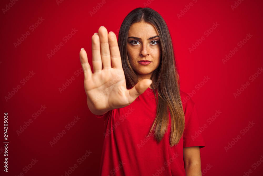 Young beautiful woman wearing t-shirt standing over isolated red background doing stop sing with palm of the hand. Warning expression with negative and serious gesture on the face. - obrazy, fototapety, plakaty 