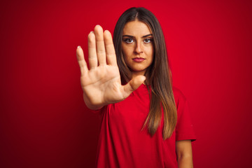 Young beautiful woman wearing t-shirt standing over isolated red background doing stop sing with palm of the hand. Warning expression with negative and serious gesture on the face.