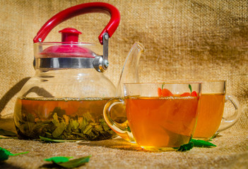 glass teapot and two cup of green tea or black tea with fresh leaves on the back of a traditional background sackcloth