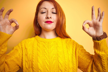 Sticker - Young redhead woman wearing winter sweater standing over isolated yellow background relax and smiling with eyes closed doing meditation gesture with fingers. Yoga concept.