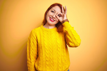 Sticker - Beautiful redhead woman wearing winter sweater standing over isolated yellow background doing ok gesture with hand smiling, eye looking through fingers with happy face.