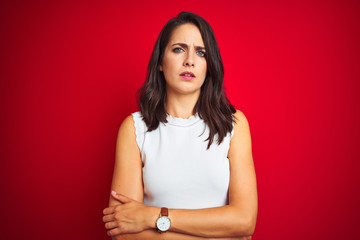 Young beautiful woman wearing white dress standing over red isolated background skeptic and nervous, disapproving expression on face with crossed arms. Negative person.