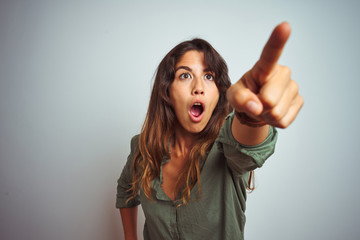 Wall Mural - Young beautiful woman wearing green shirt standing over grey isolated background Pointing with finger surprised ahead, open mouth amazed expression, something on the front