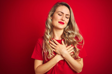 Sticker - Young beautiful woman wearing basic t-shirt standing over red isolated background smiling with hands on chest with closed eyes and grateful gesture on face. Health concept.