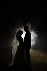 Wall Mural - silhouette of a bride and groom at night with a smokey background