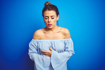 Poster - Young beautiful woman wearing bun hairstyle over blue isolated background with hand on stomach because indigestion, painful illness feeling unwell. Ache concept.