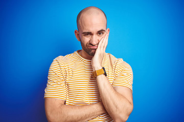 Canvas Print - Young bald man with beard wearing casual t-shirt over blue isolated background thinking looking tired and bored with depression problems with crossed arms.