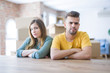 © Krakenimages.com - Young couple sitting on the table movinto to new home with carboard boxes behind them skeptic and nervous, disapproving expression on face with crossed arms. Negative person.