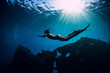 Free diver girl in pink swimwear with fins swimming underwater at wreck ship. Freediving in the ocean