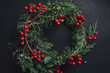 Christmas wreath detail of evergreen and berries on dark background.