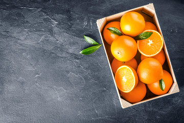 Heap oranges in wooden basket from top view. Fresh half oranges on dark stone table with leaf. Ripe tasty oranges in wooden box or basket.