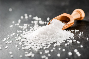 Salt in wooden scoop on dark stone table.Sea salt on black background.