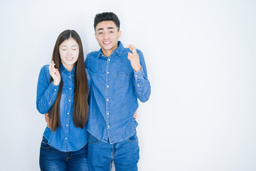 Sticker - Beautiful young asian couple over white isolated background gesturing finger crossed smiling with hope and eyes closed. Luck and superstitious concept.