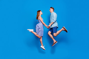 Full length body size profile side view of her she his he two nice attractive dreamy cheerful glad partners holding hand jumping having fun isolated on bright vivid shine vibrant blue color background