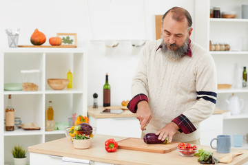 Waist up portrait of bearded senior man cooking fresh vegetable salad while standing in cozy kitchen, copy space