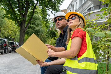 Male and female civil engineers sitting outdoors analysing projects and office blueprints