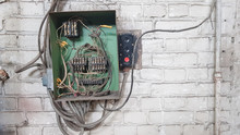 Old Electrical Panel On The Wall Of The House. Electric Cables Stick Out From The Electric Panel On The White Brick Wall Of The Old House.