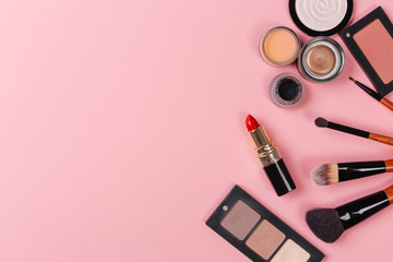 a pink makeup bag with cosmetic beauty products spilling out on to a pastel colored background, with