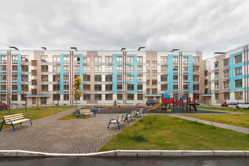 Wall Mural - Exterior of new modern low-rise house building exterior mixed-use urban multi-family residential district area development with playing field and benches for rest in foreground overcast autumn day.