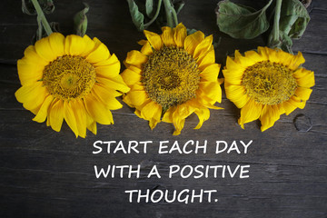 Inspirational motivational quote - Start each day with a positive thought. With yellow sun flowers on rustic wooden table background. Words of wisdom concept.