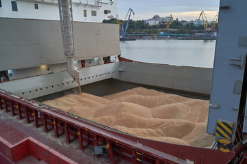 Grain loading in hold of bulk carrier ship with elevator crane closeup. Port grain elevator. Industrial sea trading port bulk cargo zone grain terminal