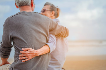 Retirement couple sitting by the sea, women embrace husbands and look at each other at the beach in the morning, life insurance plan at the retirement concept.