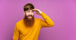© luismolinero - Redhead man with long beard over isolated purple background looking far away with hand to look something