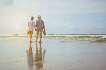 Senior couple walking on the beach holding hands at sunrise, plan life insurance at retirement concept.