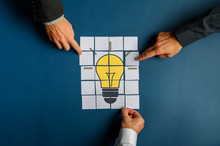 Hands Of Three Businessmen Assembling A Lightbulb Drawn On Post It Papers