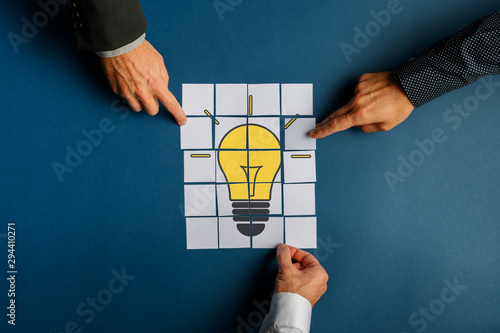 Fotografía Hands of three businessmen assembling a lightbulb drawn on post it papers