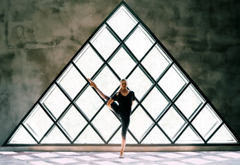 young beautiful woman doing yoga asana toe pose variation on large triangular window background
